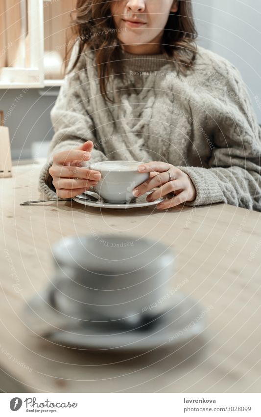 Frau hält einen Becher Latte mit einer leeren Tasse davor. Kaffee Tee Winter Herbst Pullover gesichtslos Einsamkeit gemütlich Wärme Verabredung Café Tisch