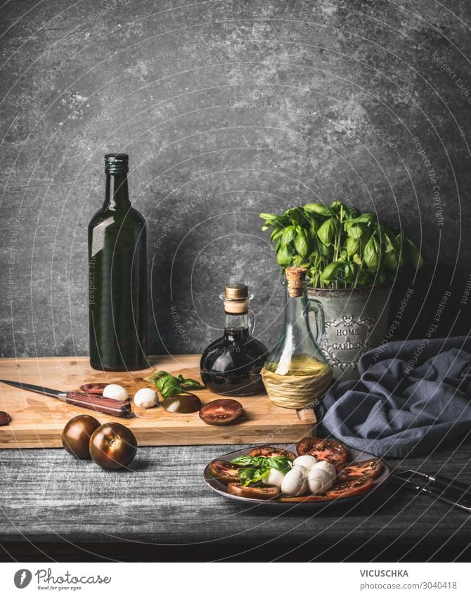 Stilleben mit italienischem Caprese-Salat, serviert auf rustikalem Tisch mit eingelegten Basilikum-Küchenkräutern und einer Flasche Olivenöl auf rustikalem Tisch mit Zutaten