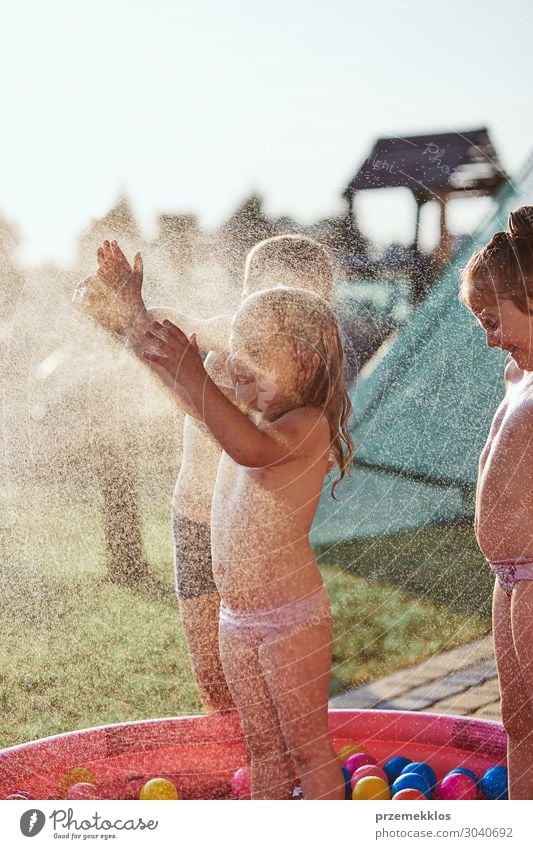 Kleine niedliche Kinder genießen ein kühles Wasser, das ihr Vater an einem heißen Sommertag im Hinterhof versprüht. Unverfälschte Menschen, echte Momente, authentische Situationen