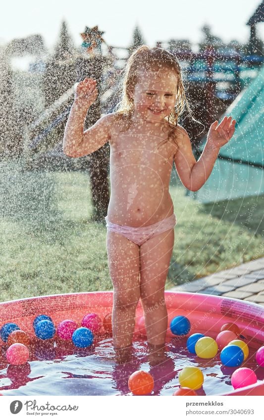 Kleine niedliche Mädchen, die ein kühles Wasser genießen, das ihr Vater an einem heißen Sommertag im Garten versprüht. Unverfälschte Menschen, echte Momente, authentische Situationen