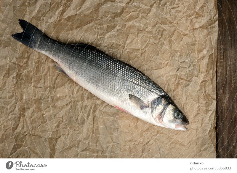 frischer ganzer Seebarschfisch auf braunem Knitterpapier Fisch Meeresfrüchte Ernährung Abendessen Tisch Küche Natur Tier Papier Holz oben grau Gesundheit Bass