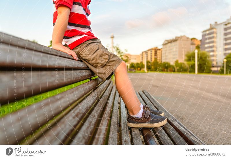 Jungenbeine, die auf der Oberseite des Bankparks sitzen, entspannen sich. Lifestyle schön Erholung Sommer Garten Kind Mensch Kindheit Fuß Natur Park Hose Schuhe
