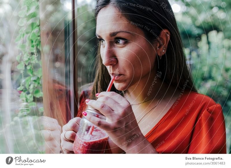 junge schöne Frau, die am Fenster steht und einen gesunden Krug Smoothie hält. Haus, Wohnung und Lebensstil Vegetarische Ernährung trinken natürlich Schminke