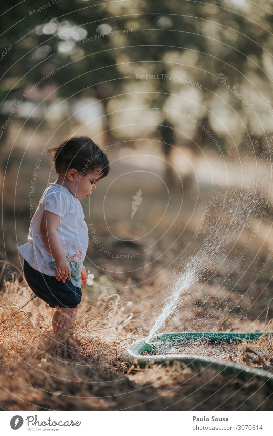 Kleines Mädchen steht bereit, wenn Wasser aus einem Schlauch an Land spritzt Kind Kindheit Sommer Sommerurlaub Sommertag Außenaufnahme Farbfoto sommerlich Natur