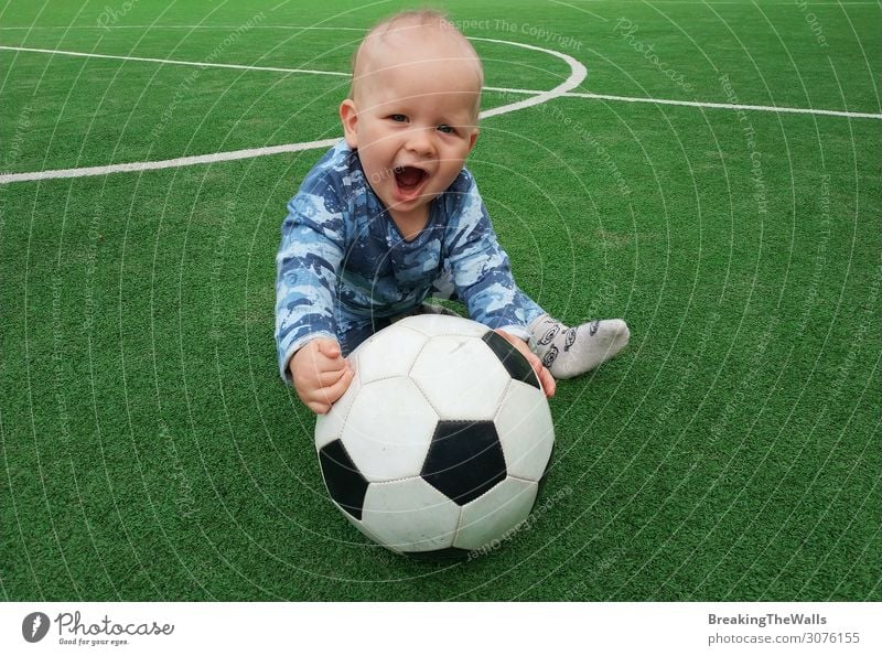 Kleiner Junge sitzt auf grünem Gras des Spielfeldes mit Fußball Fußball und Blick auf die Kamera Lifestyle Freizeit & Hobby Sport Ball Fußballplatz Stadion