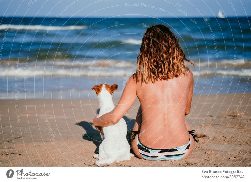 junge Frau und ihr süßer kleiner Jack-Russell-Terrier, die am Strand sitzen und sich entspannen. Sommer- und Ferienkonzept Jugendliche Erholung blau Erwachsene