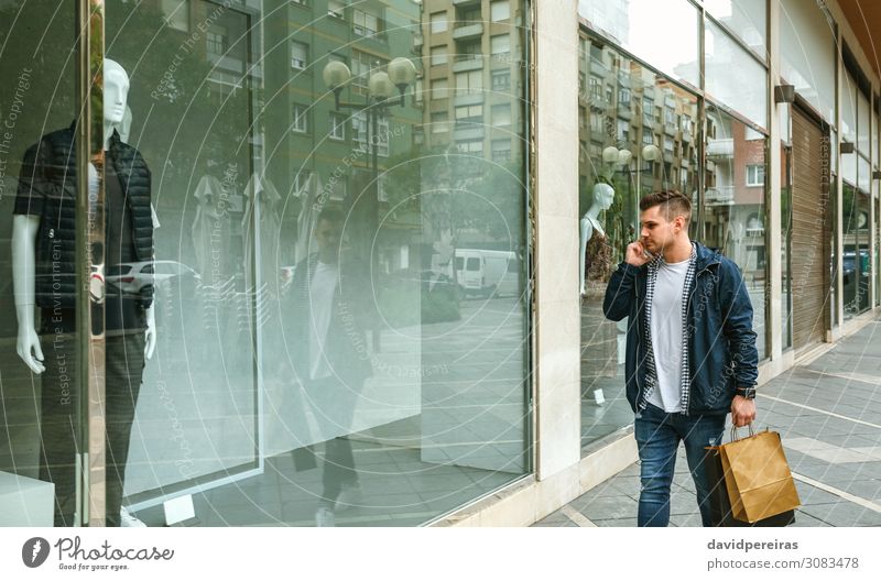 Mann mit Einkaufstaschen im vorderen Bekleidungsgeschäft Lifestyle kaufen Stil sprechen PDA Mensch Erwachsene Mode Jeanshose authentisch jung laufen Ladenfront