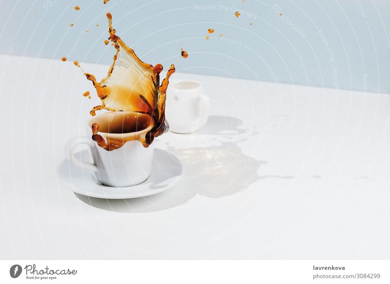 Nahaufnahme der Tasse mit spritzendem Kaffee, Untertasse und Milchkännchen Pastellton blau Bewegung Tee Lebensmittel Foodfotografie Frühstück schwarz Tropfen