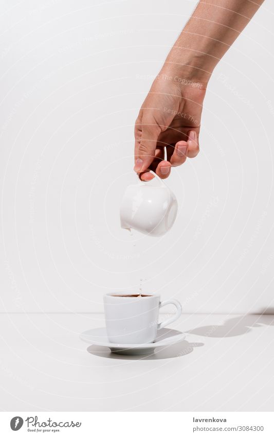 Frauenhand, die Mandelmilch in eine Tasse Kaffee gießt. Getränk Frühstück Koffein Keramik Milchkännchen frisch Hand heiß Morgen Becher Untertasse Tee weiß