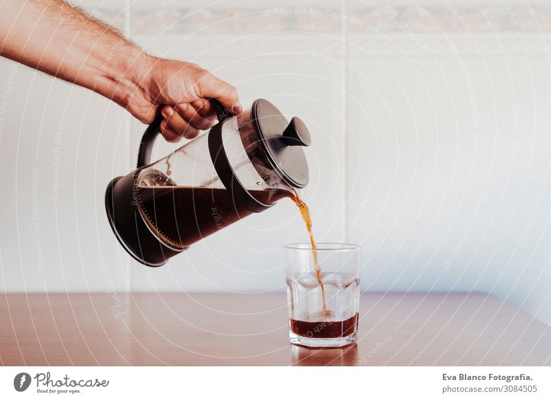 kaukasischer Mann, der Kaffee in einem transparenten Glas serviert. Frühstück Getränk Geschirr Löffel Lifestyle kaufen Erholung Freizeit & Hobby Haus Tisch