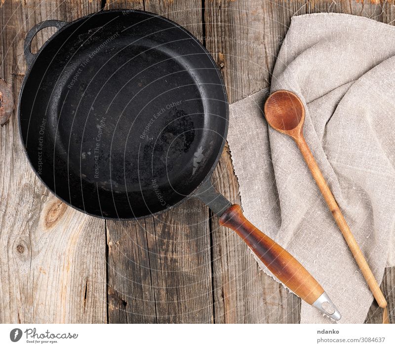 leere schwarze runde Bratpfanne mit Griff und Löffel Pfanne Tisch Küche Werkzeug Holz Metall alt oben Sauberkeit braun grau Hintergrund Holzplatte gießen