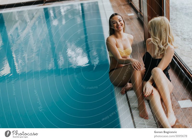 Attraktive junge Frauen im Bikini sitzen am Pool. Lifestyle Glück schön Körper Wellness Erholung Schwimmbad Freizeit & Hobby Winter Mensch Erwachsene