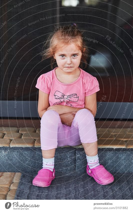 Kleines trauriges Mädchen, das weint, weil sie ihr Spielzeug verloren hat und auf einer Stufe auf der Terrasse sitzt. Echte Menschen, authentische Situationen