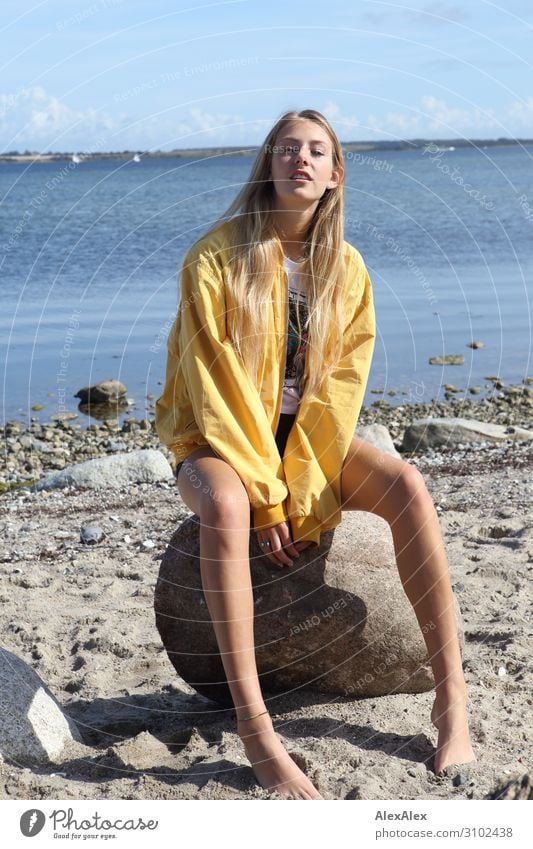 Junge Frau mit gelber Jacke sitzt am Strand Lifestyle Freude schön Leben Sommer Sonne Sonnenbad Meer Jugendliche Beine 18-30 Jahre Erwachsene Schönes Wetter