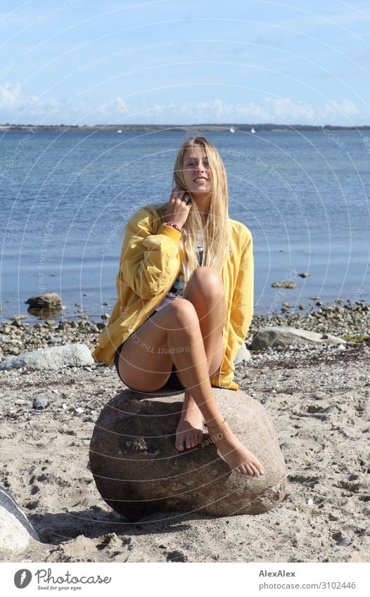 Junge Frau mit gelber Jacke sitzt auf Felsen am Strand Stil Freude schön Leben Wohlgefühl Sommer Sommerurlaub Sonne Meer Jugendliche Beine 18-30 Jahre