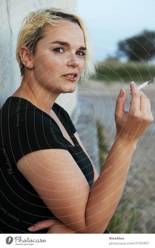 Junge Frau sitzt auf einem Block und raucht eine Zigarette Stil schön Jugendliche 18-30 Jahre Erwachsene Sommer Schönes Wetter T-Shirt Piercing blond kurzhaarig