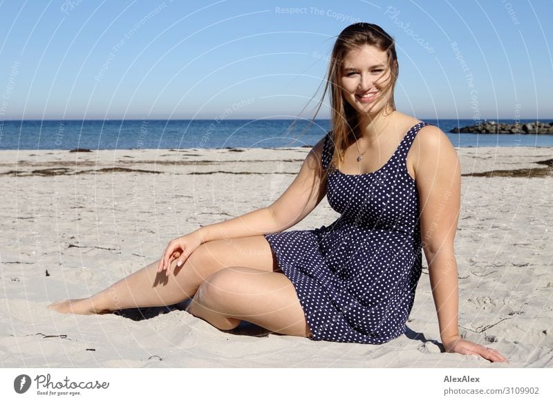 Junge, große Frau sitzt im Sommerkleid am Ostseestrand und lächelt Stil schön Wellness Wohlgefühl Sommerurlaub Sonne Sonnenbad Strand Meer Junge Frau