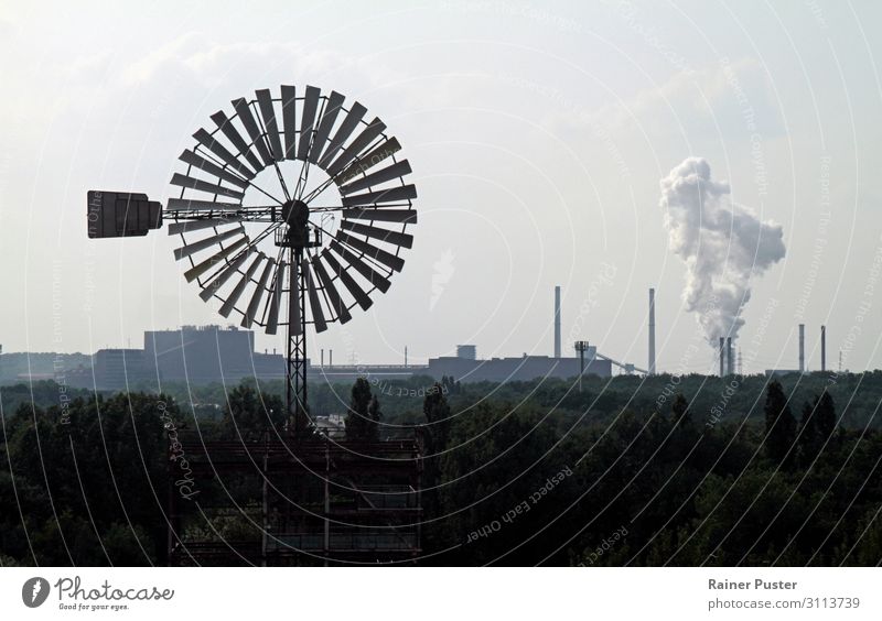 Ein Windrad dreht im Wind vor einem Hintergrund mit Schornsteinen und Industrie. Fabrik Energiewirtschaft Erneuerbare Energie Windkraftanlage Wolkenloser Himmel