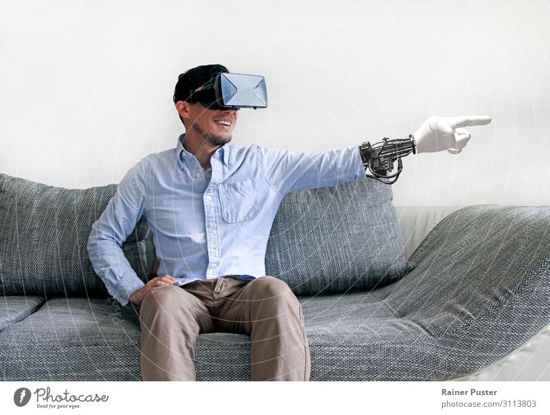 Mann auf dem Sofa mit Virtual-Reality-Brille und virtuellem Arm Wirtschaft Medienbranche Telekommunikation sprechen Headset Computer Hardware VR-Brille maskulin