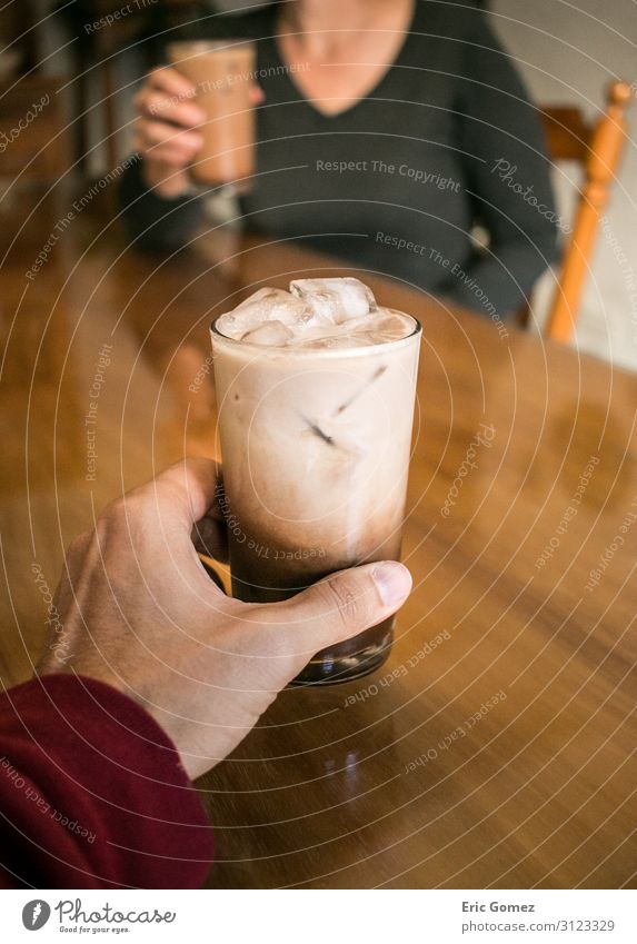 Hand hält Kaffee, Frau trinkt im Hintergrund Kaffeetrinken Erfrischungsgetränk Milch Espresso Glas Lifestyle Freude Junger Mann Jugendliche Erwachsene 2 Mensch