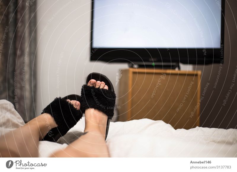 Der Mensch sieht nachts im Bett mit schwarzen Flip Flops fern. Getränk Freude Erholung Freizeit & Hobby Sofa Tisch Schlafzimmer Entertainment Bildschirm
