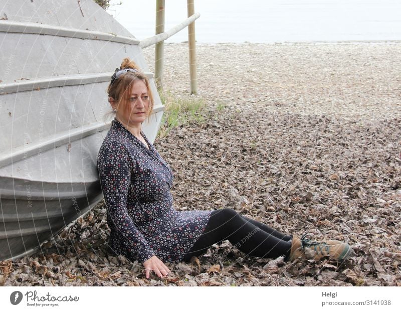 Frau mit brünetten hochgesteckten Haaren sitzt im Laub vor einem umgekippten Boot Mensch feminin Erwachsene 1 45-60 Jahre Umwelt Natur Landschaft Frühling Blatt