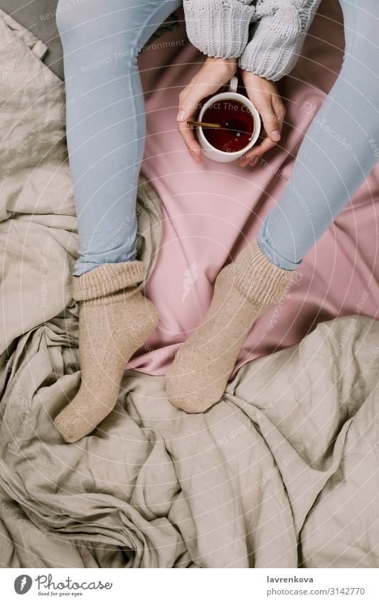 Gemütliches Flachlegen der Frauenbeine in blauen Leggins und warmen Socken. Herbst Schlafzimmer Getränk Decke Bettdecke Bekleidung kalt Geborgenheit gemütlich