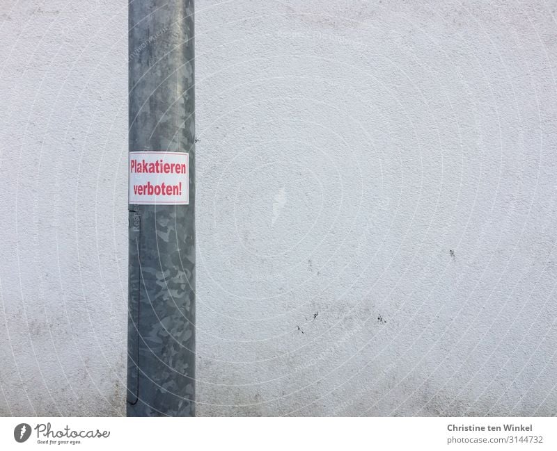 Laternenpfahl mit Aufkleber 'Plakatieren verboten' vor einer schmutzigen weißen Wand Mauer Beton Metall Schilder & Markierungen Hinweisschild Warnschild