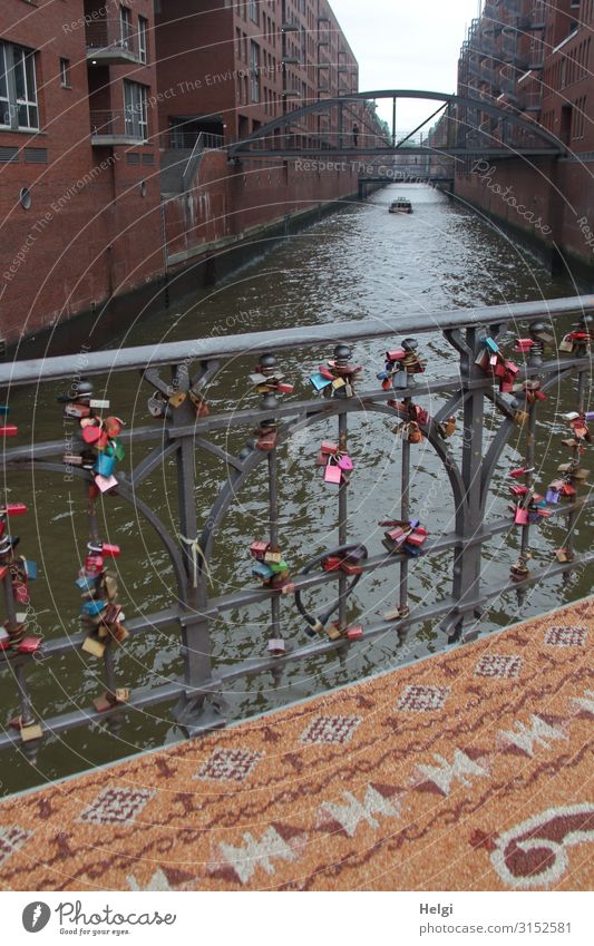 Brückengeländer mit vielen Liebesschlössern, davor ein gemusterter Teppich aus kleinen Steinen in der Speicherstadt Hamburg Wasser Hafenstadt Gebäude