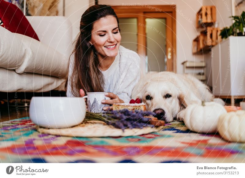 schöne Frau und süßer Golden Retriever-Hund, der zu Hause ein gesundes Frühstück genießt, auf dem Boden liegend. gesundes Frühstück mit Tee, Früchten und Süßigkeiten. Herbstzeit