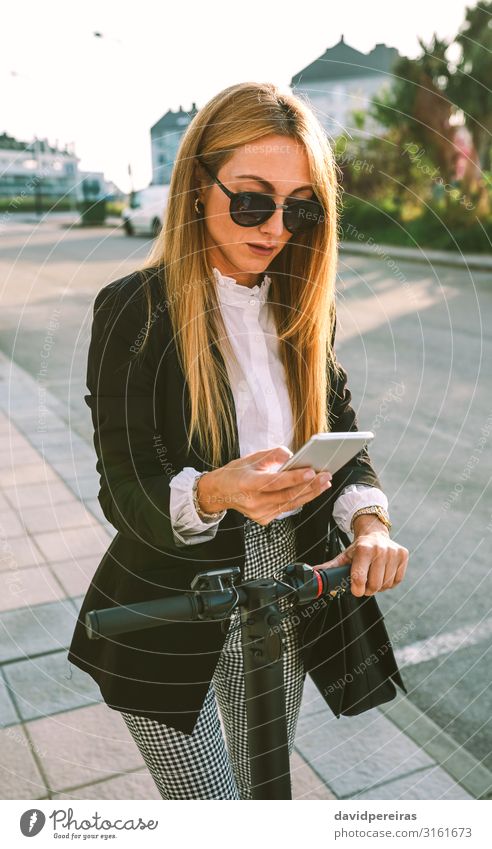 Geschäftsfrau mit E-Scooter beim Blick auf das Handy elegant Stil schön Business PDA Mensch Frau Erwachsene Verkehr Straße Mode Sonnenbrille modern E-Roller