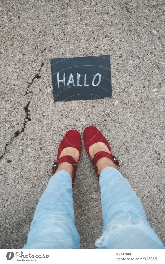 frau steht vor einer kleinen tafel mit dem wort "hallo" darauf geschrieben .. Frau weiblich Beine Füße Schuhe Jeans stehen Straße Asphalt Tafel Geschriebenes