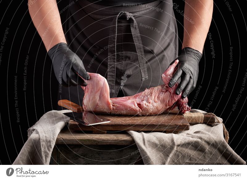 der Koch in schwarzen Latexhandschuhen hält einen ganzen Kaninchenkadaver Fleisch Ernährung Abendessen Messer Tisch Küche Mann Erwachsene Hand Handschuhe Holz