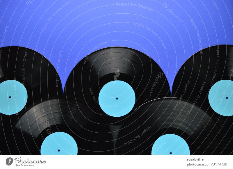 fünf alte schwarze Vinyl Schallplatten aufeinander gelegt mit leerem türkis farbenem Label auf blauem Hintergrund als Band unten mit Freiraum für Text oben| Symmetrie