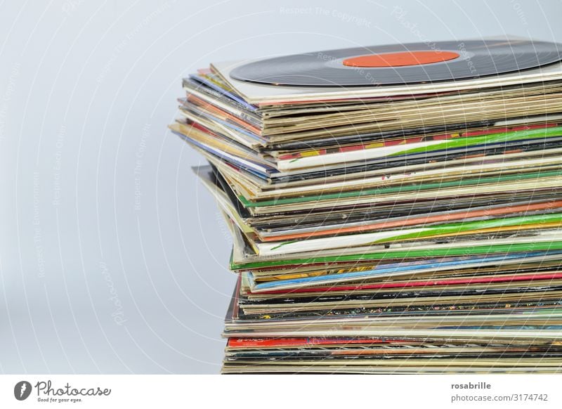 Stapel mit vielen alten bunten Vinyl Schallplattenhüllen aufeinander mit einer schwarzen Schallplatte oben drauf mit neutralem orangenem Label vor weißem Hintergrund mit Freifläche für Text links | alt