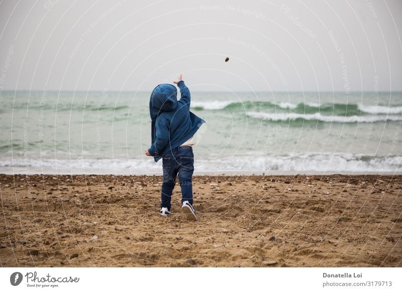 Kind wirft einen Stein ins Meer Leben Spielen Strand Wellen Winter Mensch maskulin Kindheit Körper 1 1-3 Jahre Kleinkind Herbst Jeanshose Sand blau Lebensfreude
