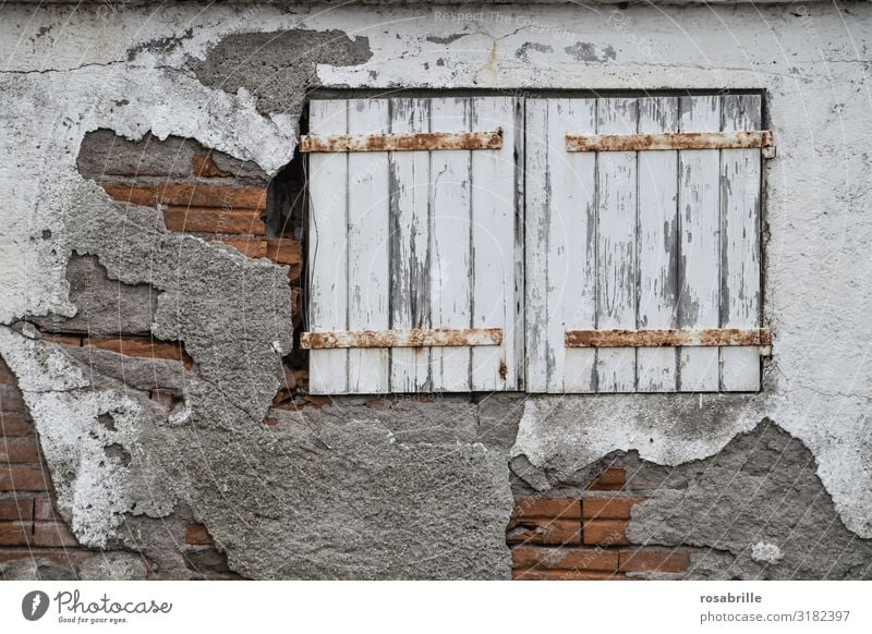 alte geschlossene Fensterläden mit abblätterndem weißem Lack und verrosteten Scharnieren in Backsteinfassade mit teilweise fehlendem Putz die schon bessere Tage gesehen haben | alt