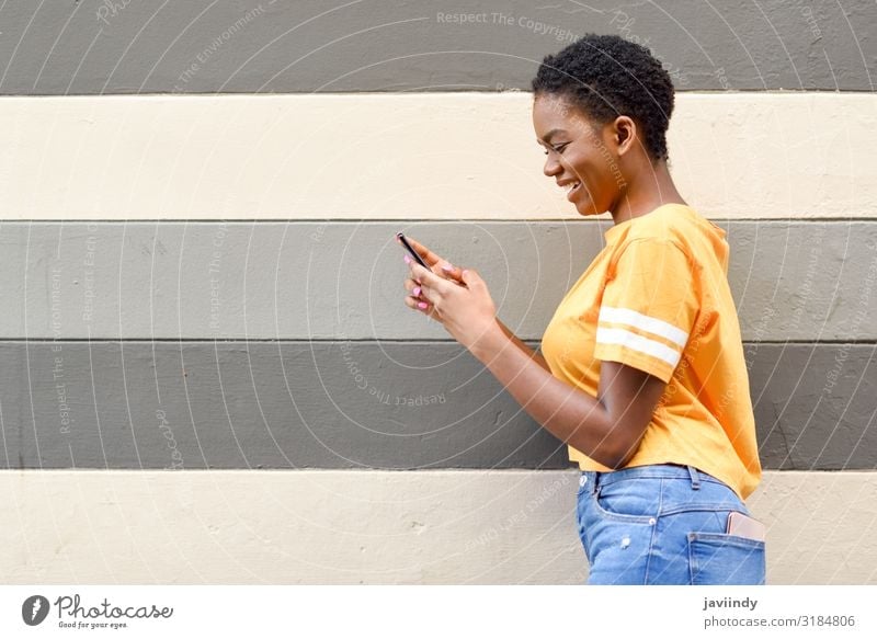 Junge schwarze Frau, die lachend ihr Smartphone im Freien benutzt. Lifestyle Stil Freude Glück Haare & Frisuren Telefon Funktelefon PDA Technik & Technologie