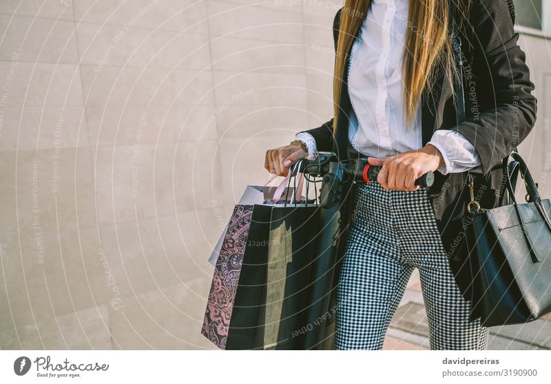 Unkenntliche Frau mit Einkaufstaschen auf Elektroroller kaufen elegant Stil Mensch Erwachsene Hand Verkehr Straße Mode Hemd blond modern Schwarzer Freitag