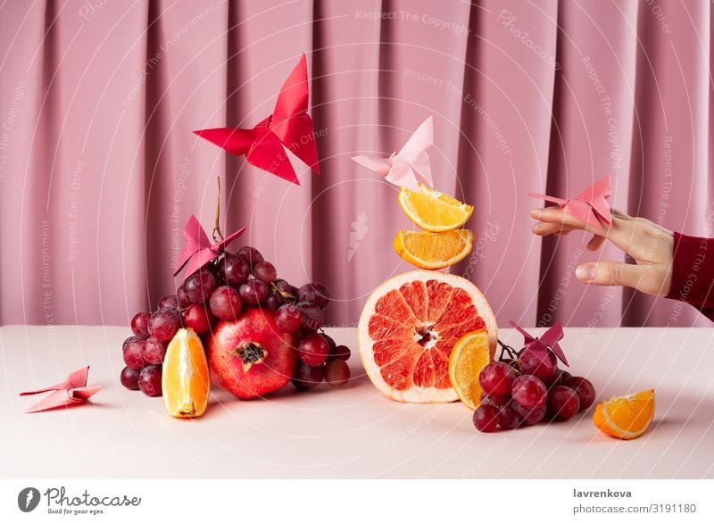 Verschiedene Früchte auf rosa Tisch mit Origame-Papier-Schmetterlingen Frühstück Zitrone Zitrusfrüchte Diät Lebensmittel Gesunde Ernährung Foodfotografie frisch
