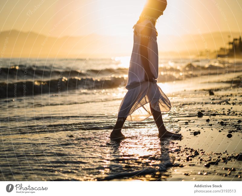 Liebenswertes Mädchen, das bei Sonnenuntergang am Meer spazieren geht. Seeküste laufen reizvoll Küste Strand Sommer Wasser Sonnenstrahlen Kind Kindheit Glück
