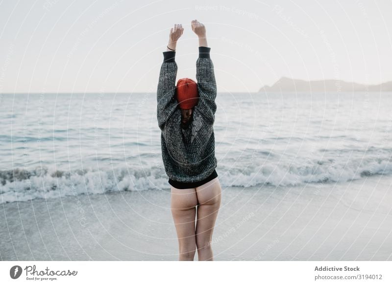 Nicht erkennbare Frau, die die Freiheit in der Nähe des wogenden Meeres genießt. Wellen Gesäß angehoben Hände hoch Unwetter Natur Wasser nackt Pullover Hut