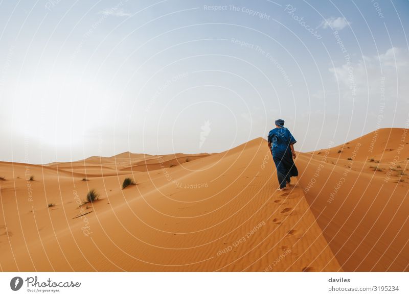 Ein arabischer Mann in blauer Kleidung läuft auf einer Wüstendüne. Lifestyle exotisch Ferien & Urlaub & Reisen Tourismus Ausflug Abenteuer Expedition Sonne