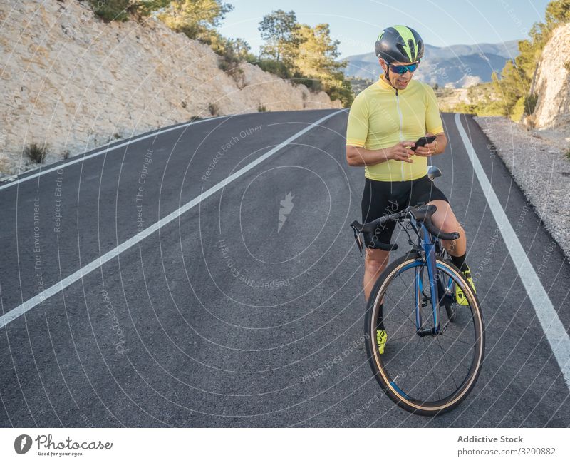 gesunder Mann mit Smartphone nach dem Radfahren auf einer Bergstraße an einem sonnigen Tag Freizeit & Hobby Athlet Sport Ausritt Fahrrad Rennsport