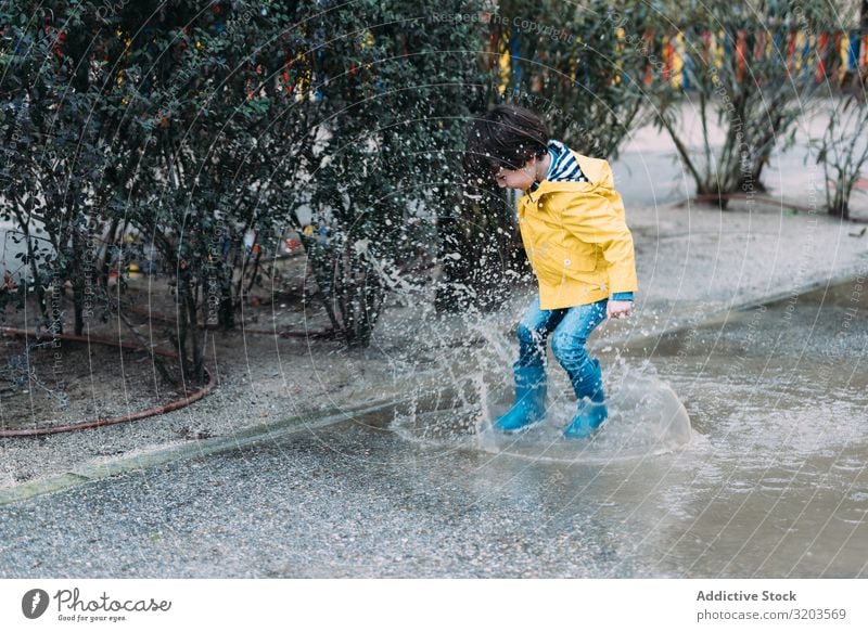 Glückliches Kind springt auf Pfütze Junge springen Freude Straße Gummistiefel nass Wasser spielerisch Kindheit Herbst Wetter Natur Spielen Regenmantel
