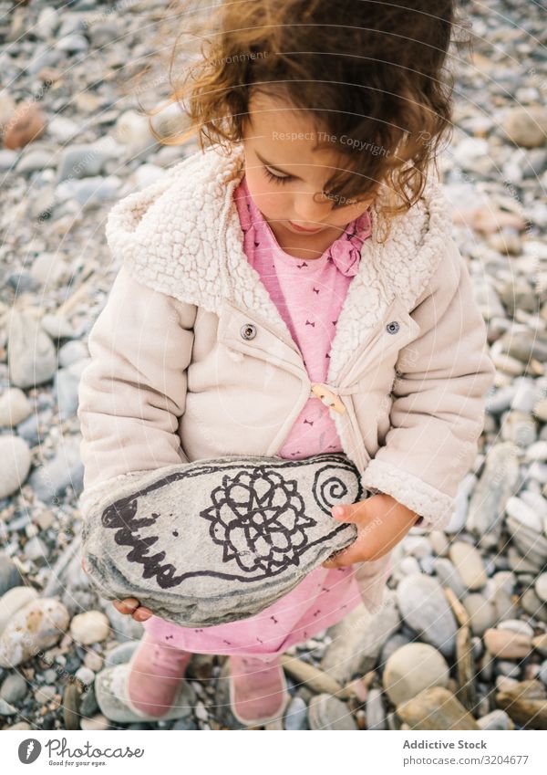 Mädchen hält bemalten Stein beim Spielen am Strand Kleinkind Interesse niedlich Kindheit Seeküste Verstand Kreativität Gelassenheit Küste