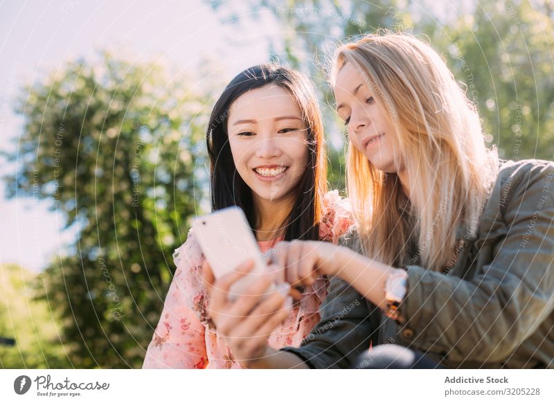 Freundinnen, die im Park ein Smartphone benutzen Freundschaft PDA benutzend zeigen Lächeln Person gemischter Abstammung Frau Jugendliche Mitbenutzung