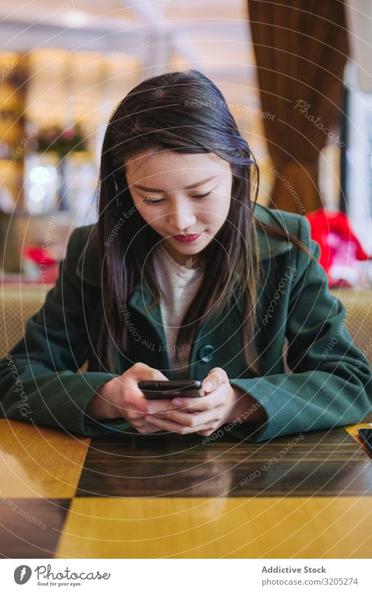Asiatische Frau mit Smartphone im Café PDA benutzend sitzen Tisch asiatisch gemütlich Lifestyle Freizeit & Hobby urwüchsig ruhen Erholung Stil trendy elegant