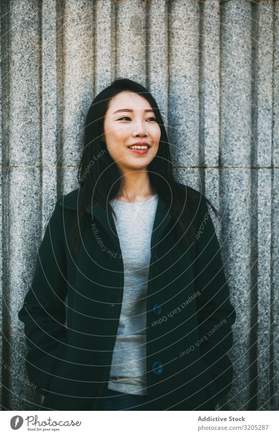 Asiatische Frau an Marmorwand Wand anlehnen asiatisch Lächeln Jugendliche Straße Großstadt Gebäude elegant Mantel Stil trendy lässig urwüchsig Außenseite