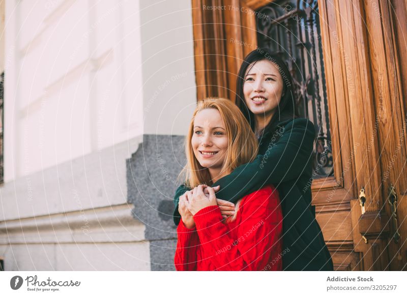 Fröhliche Freundinnen umarmen sich in der Nähe einer Ziertür Freundschaft Umarmen Lächeln Wegsehen Tür Straße Gebäude Großstadt Person gemischter Abstammung